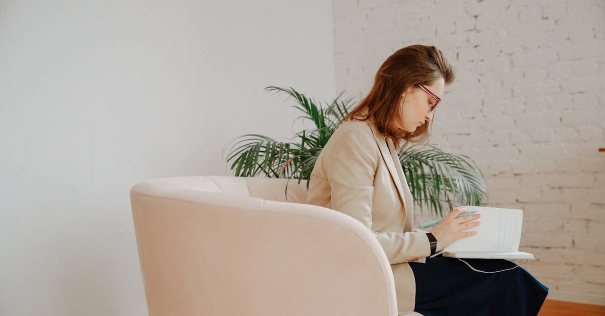 A woman sits across from her therapist during a CBT session, writing in a journal as they review her thought record together.